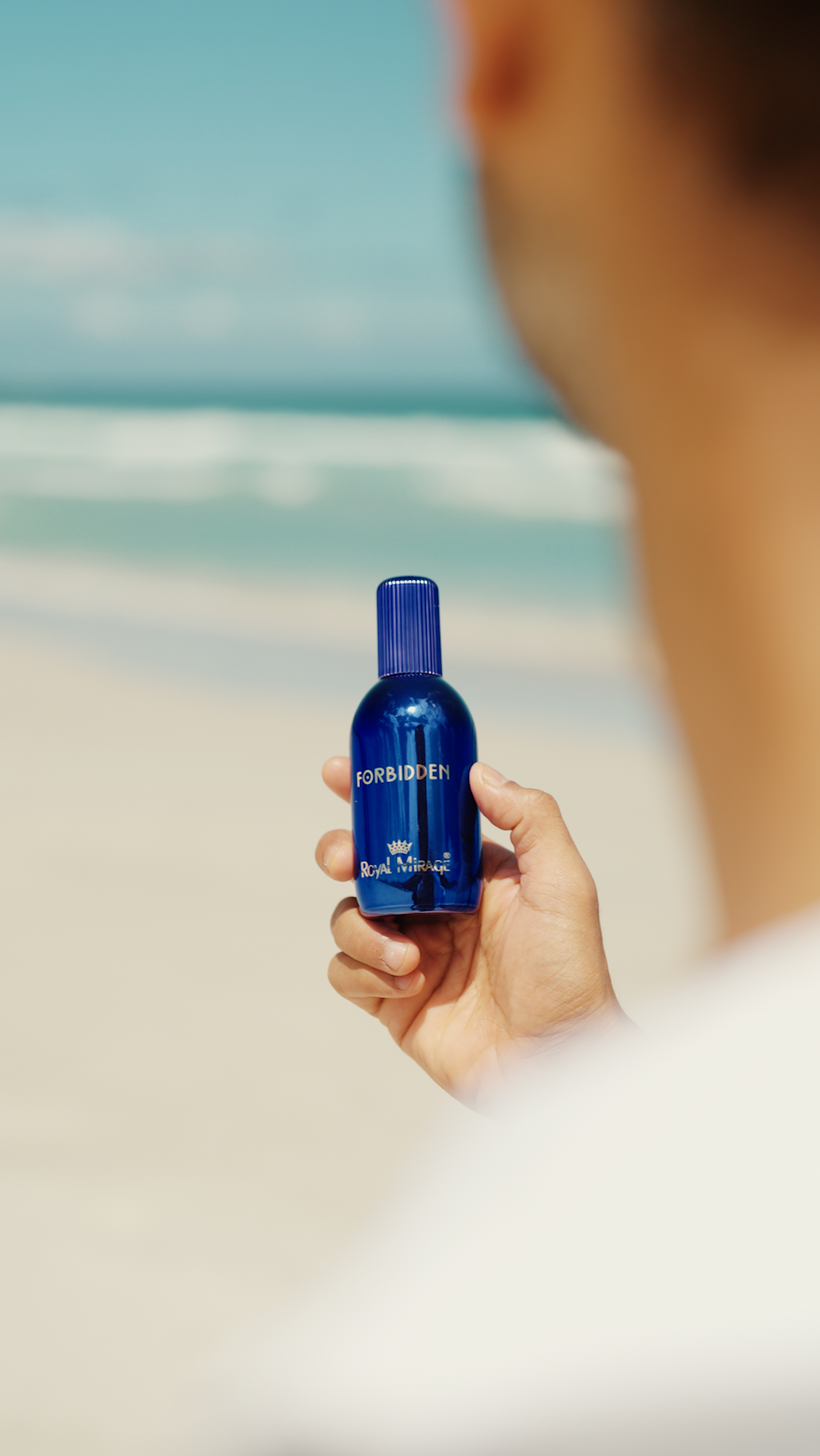 Person holding a blue bottle with a blurred beach background